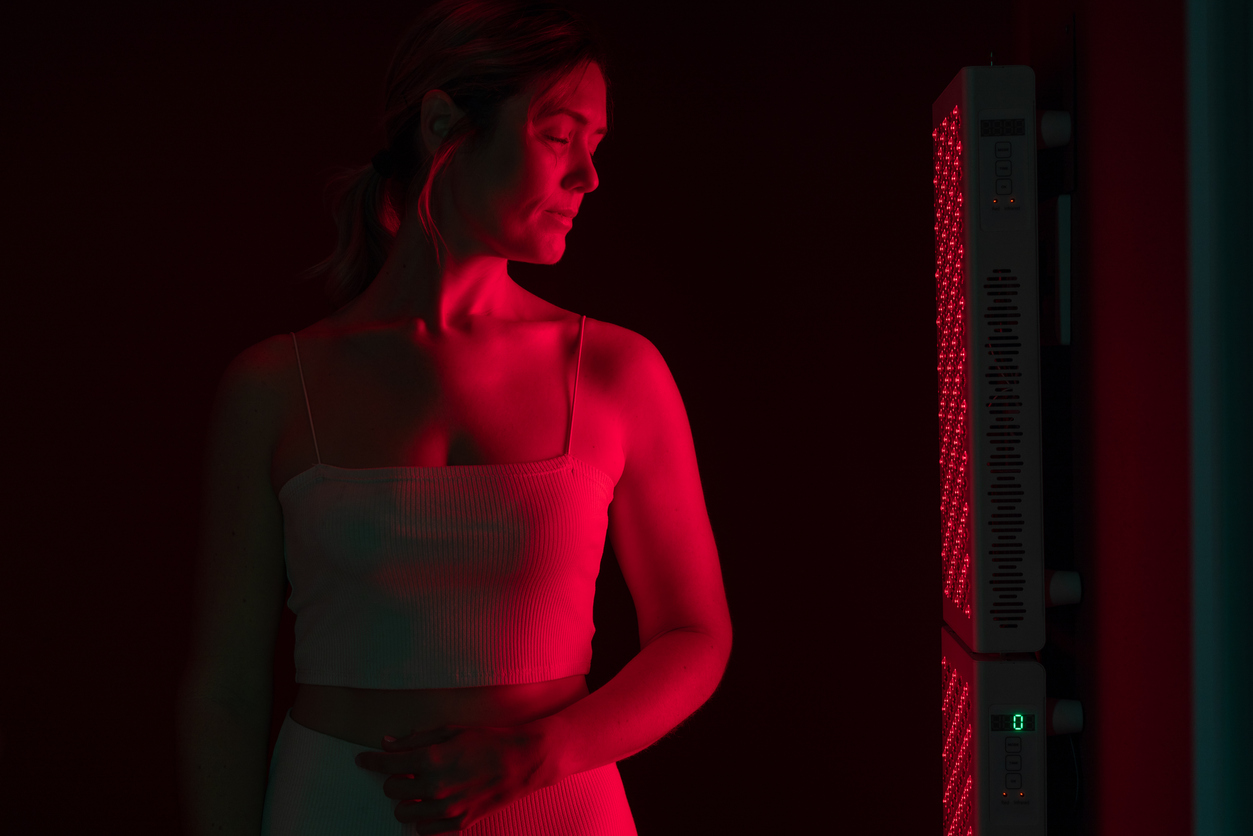 Mature woman receiving red light therapy. Woman standing next to a red light device in a beauty spa. Anti-aging and skin care treatment.