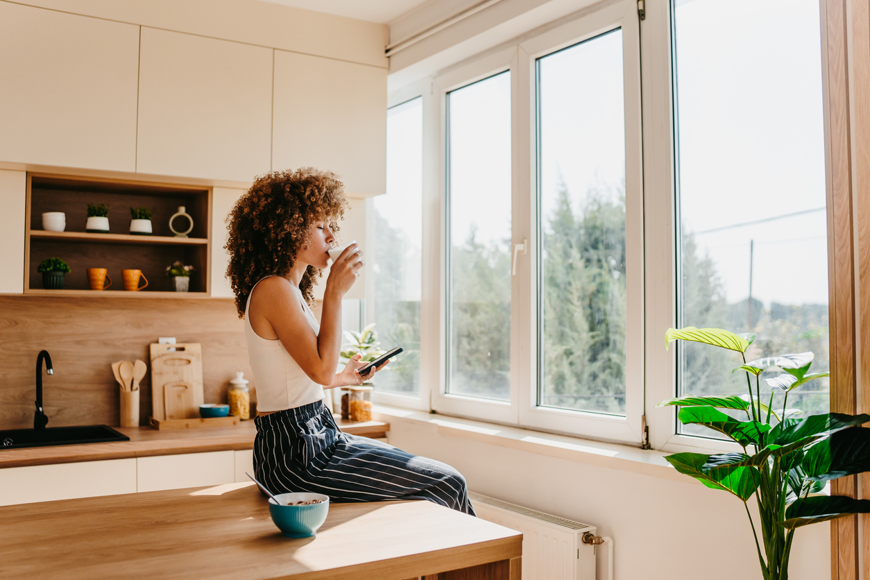 Serene morning routine of a young woman drinking coffee and using smartphone in a modern kitchen